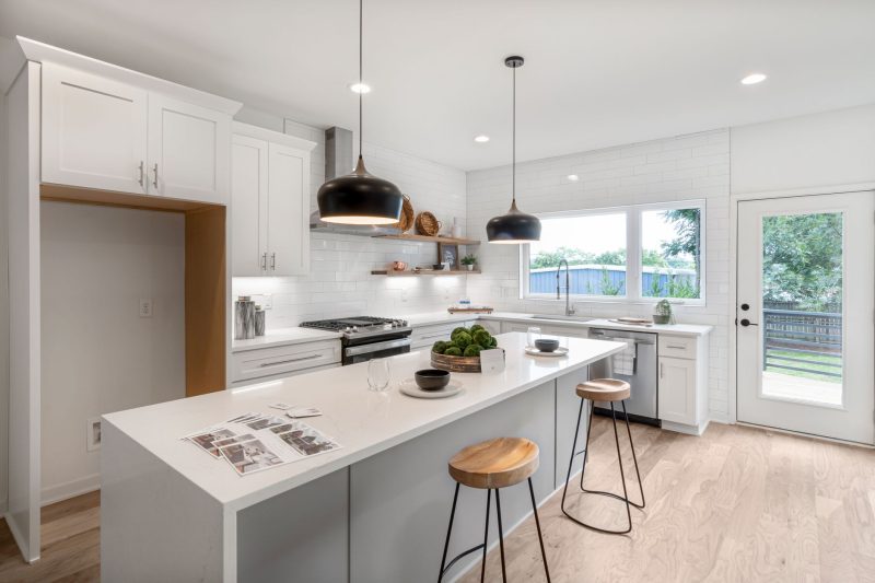 Bright modern kitchen with white cabinetry, wooden stools, and pendant lighting
